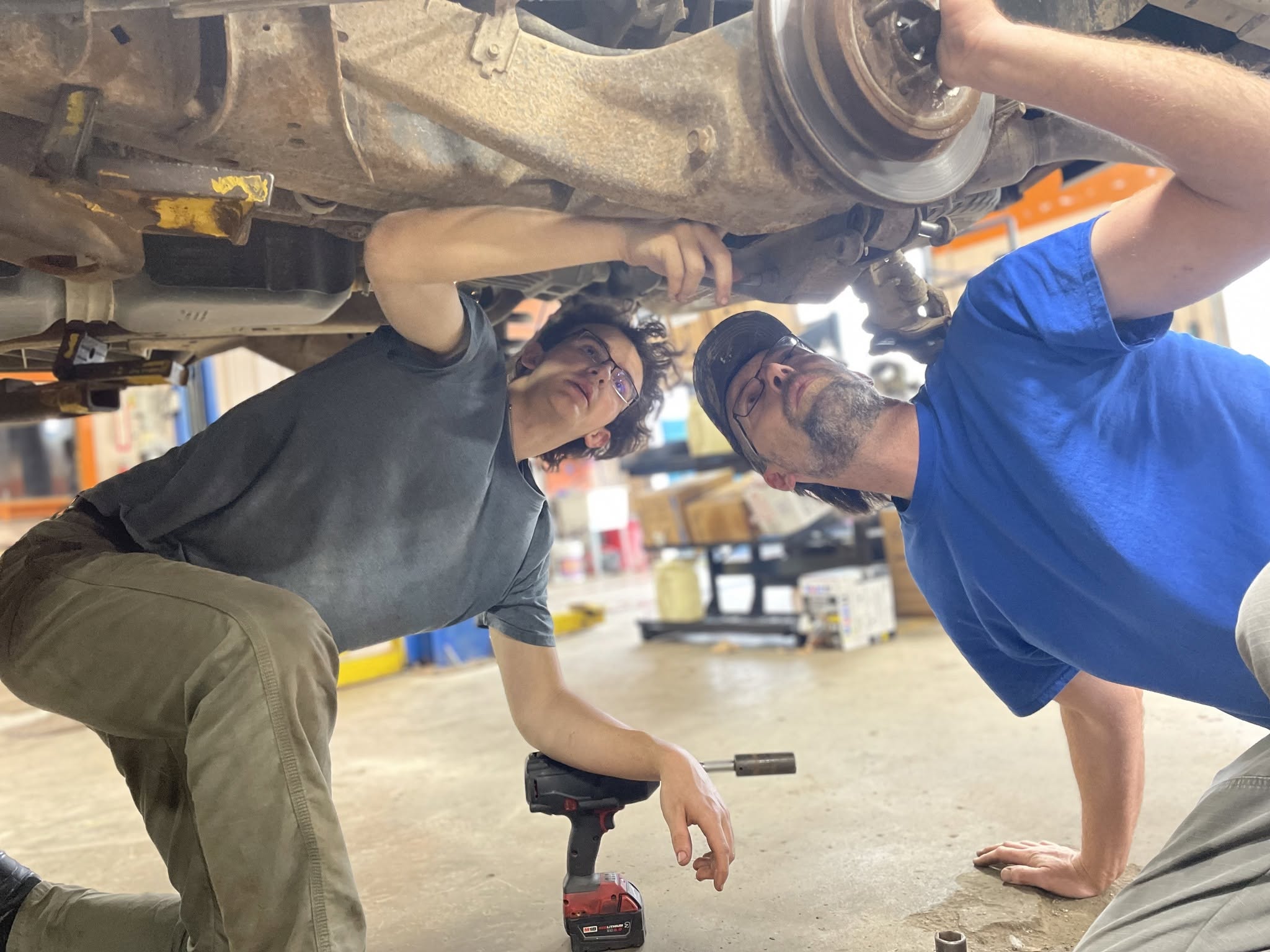 Two Steuben Automotive technicians working underneath a lifted vehicle in the shop bay